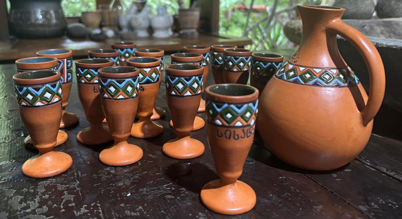 A selection of traditional, handmade Georgian ceramic cups and a vase featuring blue, green and white paint details
